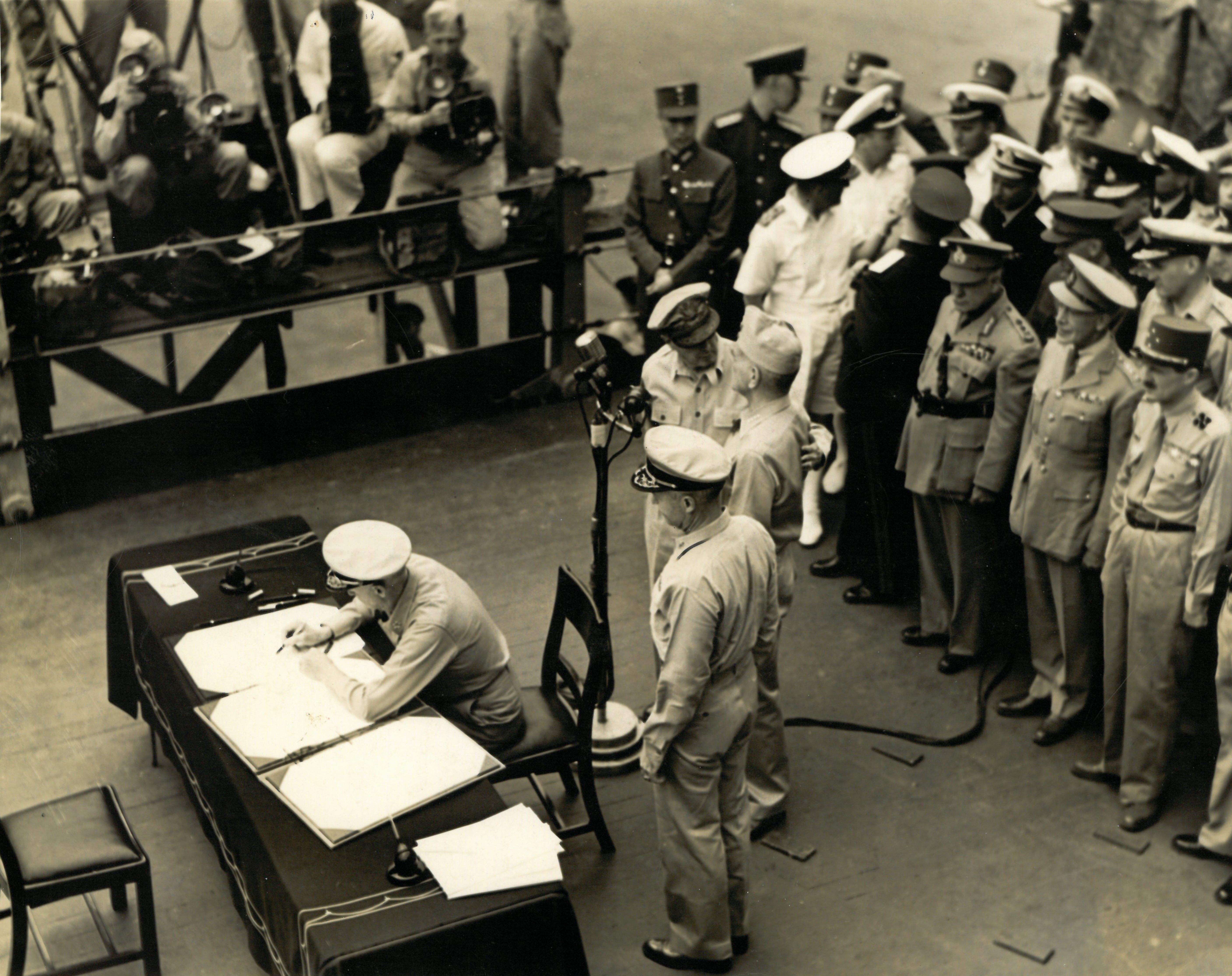 Official US Navy photograph of Admiral Chester W. Nimitz signing the Instrument of Surrender.  General Douglas MacArthur and Admiral William Halsey are standing behind the microphone.  The USS Missouri was Admiral Halsey's flagship.